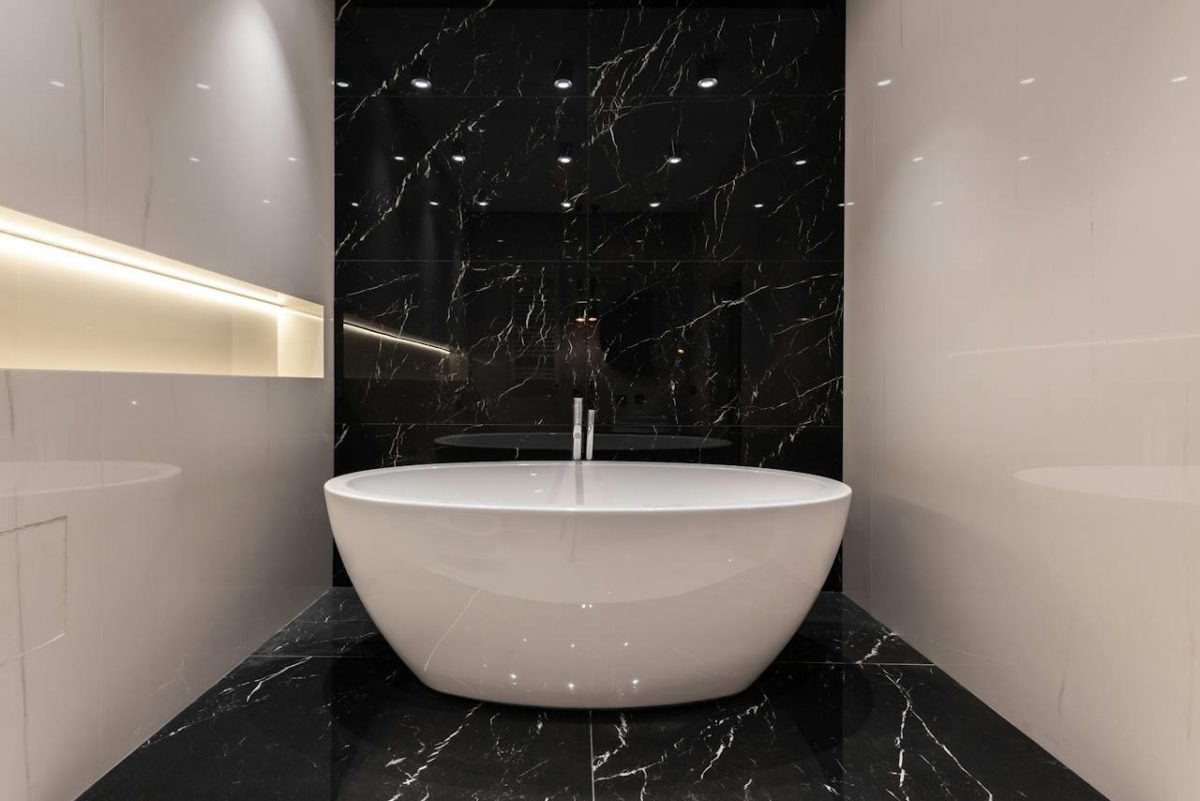 bathroom with white tub and black and white marble walls